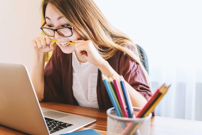 mulher em frente ao computador, ela esta usando oculos e esta mordendo um lapis entre os dentes, mostrando frustação